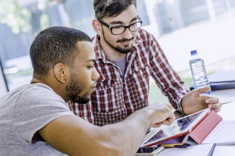 Two men studying with a tablet screen in front of them.